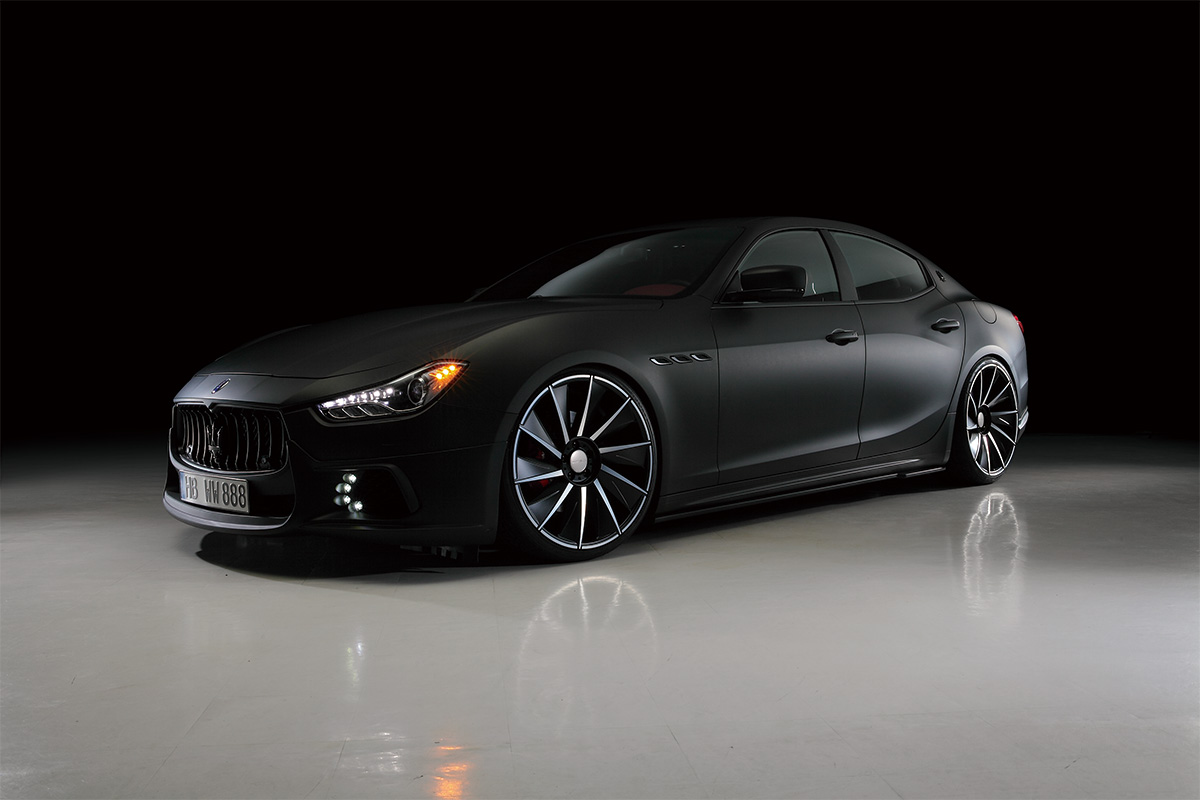 Matte black Maserati Ghibli on large black and polished forged wheels in a dark studio