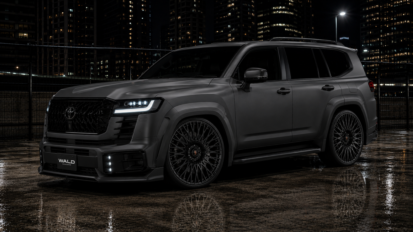 Matte grey Toyota Land Cruiser LC300 with a WALD International body kit and black multi-spoke forged wheels at night